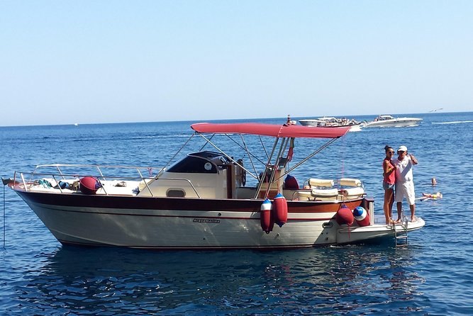 A gozzo at anchor under a red canopy with the Amalfi Coast running away behind it