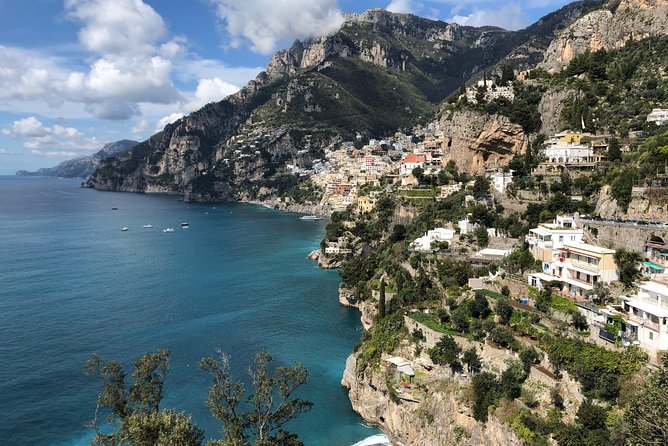 A green headland dropping into deep blue water with villas cut into the terraces below the ridge