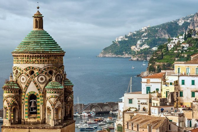 A majolica-tiled bell tower in green and yellow glaze above an Amalfi Coast harbour