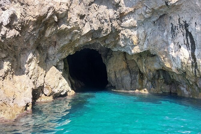 The mouth of a sea cave in the limestone with the water inside lit turquoise from below