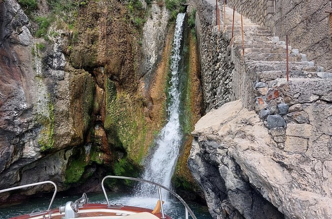 A waterfall dropping through a rock inlet on the coast with a stone stair cut beside it